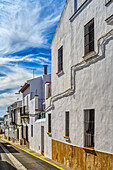 A picturesque street in Carrion de los Cespedes, Sevilla, showcasing traditional whitewashed buildings under a vibrant blue sky. Perfect representation of Spanish village charm.