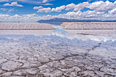 Piles of salt at a salt mining operation on the salt flats of Salinas Grandes in northwest Argentina. Clouds are reflected on a shallow sheet of water.