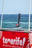 Windsurfing competition in El Medano, Tenerife with vibrant banners promoting the 2024 World Windsurfing Championship. Energetic scene capturing sport and coastal excitement.