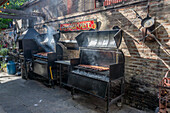 Sausages cooking over coals in wood-fired grills in the outdoor kitchen of a parrilla in Caminito, La Boca, Buenos Aires, Argentina.