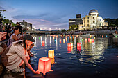 Woman float lanterns on the river, in front of Atomic Bomb Dome with floating lamps on Motoyasu-gawa River during Peace Memorial Ceremony every August 6 in Hiroshima, Japan