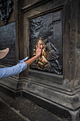 Tourists touching a plaque that is part of the statue St. John of Nepomuk for good luck, Prague.