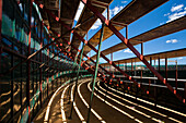 A view under empty stands of a portable bullring in Aznalcazar, Seville, Spain. The structure is highlighted by shadows and sunlight, creating a geometric pattern.