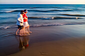 Long exposure captures two elderly women enjoying a serene walk by the ocean at Punta Umbria beach in Huelva, Andalusia, Spain during a beautiful sunset.