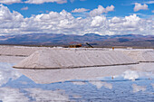 Piles of salt at a salt mining operation on the salt flats of Salinas Grandes in northwest Argentina. Clouds are reflected on a shallow sheet of water.