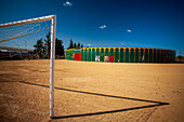 A unique view of a portable bullring set up in Aznalcazar, Seville, Spain, with a football goal in the foreground under a clear blue sky.