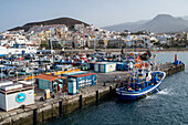 Scenic view of colorful fishing boats docked at Los Cristianos Seaport in Tenerife, Spain, with mountains and town in the background.