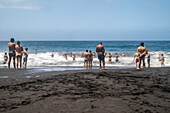 A group of bathers enjoying the waves at Bollullo Beach on the northern coast of Tenerife, La Orotava, Canary Islands, Spain. Long exposure.