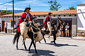 Gauchos in traditional red Salteño ponchos riding on horseback in a parade in Cachi, Argentina. Cowhide guardemontes protect the rider from thorn bushes common in the area.