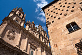 Side view of La Casa de las Conchas and the Clerecía Church along the street in Salamanca, highlighting architecture under a bright sky.