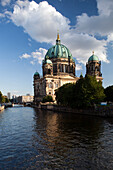 The Berliner Dom stands majestically alongside the Spree River, showcasing its stunning architecture beneath a clear blue sky.