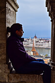 Young woman enjoying the view of Parliament building, Chain Bridge and Danube River through old columns, Budapest, Hungary, Europe