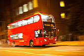 A double decker bus speeds through London streets, illuminated by city lights, showcasing the vibrant atmosphere of the UK capital at night.