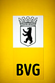 The coat of arms featuring a bear and BVG logo are displayed prominently on a yellow tram in Berlin, Germany, showcasing public transit.