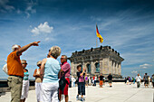 Tourists gather on the Reichstag\'s roof terrace in Berlin, admiring the cityscape and the German flag flying overhead.