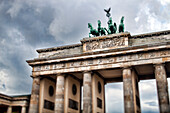 Tourists explore the iconic Brandenburg Gate in Berlin, appreciating its grand architecture and historical significance on an overcast day.