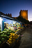 Vibrant street stalls display a variety of fruits as dusk settles over Chefchaouen, showcasing the local market life by the Kasbah.