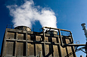 Steam rises from cooling towers at a chemical factory in Huelva, Andalusia, showcasing industrial activity under a clear blue sky.