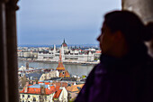 Young woman enjoying the view of Parliament building, Chain Bridge and Danube River through old columns, Budapest, Hungary, Europe