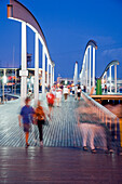 Visitors stroll along the Pasarela del Maremagnum, enjoying the vibrant atmosphere by the waterfront during a lively evening.