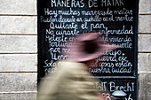 A man with a hat strolls by a wall featuring Bertolt Brechts poem on Tallers Street, Barcelona, reflecting on the art of expression.