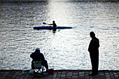 Two fishermen enjoy their day along the Guadalquivir River while a kayaker paddles past under the Triana Bridge in Sevilla.