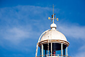 The old lighthouse stands tall at Bonanza port, showcasing its weather vane against the vibrant blue sky of Sanlucar de Barrameda.