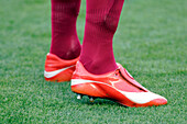 Close up view of vibrant red soccer cleats worn on a lush green field, highlighting sports and athleticism.