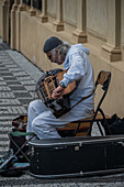 Street musician playing the hurdy-gurdy in a square at Prague Castle complex