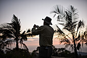 Mann beim Fotografieren mit einem Smartphone bei Sonnenuntergang in der Sierra Nevada de Santa Marta, Kolumbien