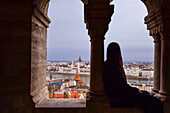 Young woman enjoying the view of Parliament building, Chain Bridge and Danube River through old columns, Budapest, Hungary, Europe