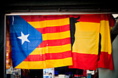 Catalan and Spanish flags hang side by side in a Las Ramblas shop, symbolizing cultural and political identity in Barcelona, Spain.