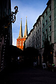 The historic Nikolaikirche stands prominently at the end of a serene street in Berlin, illuminated by the fading evening light.