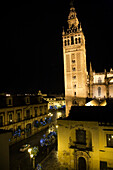 The Giralda stands illuminated at night next to the Archbishops Palace in Seville, showcasing the beauty of the historic architecture.