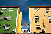 Brightly colored buildings in the Pío XII neighborhood display drying laundry under a clear blue sky in Sevilla.