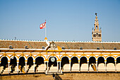 Die Stierkampfarena Maestranza zeigt ihre ikonische Architektur unter klarem Himmel, mit der wehenden Fahne auf der Spitze und dem Turm im Hintergrund