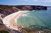 A stunning beach by Sagres in the Costa Vicentina, filled with sunbathers and surfers enjoying the clear blue waters.