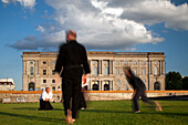 Martial artists engage in judo and karate on the green lawn of Schlossplatz, surrounded by historic architecture in Berlin, Germany.