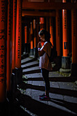 Young caucasian woman praying at Fushimi Inari Taisha temple at night, Kyoto, Japan