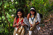 Kogi mamo (priest) and family walking through the forest, with elderly woman sewing while walking.