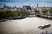 A busy Thames River teems with boats, with Hungerford Bridge gracefully arching in the background, showcasing Londons vibrancy.