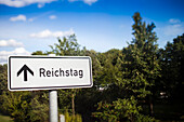 A sign points the way to the Reichstag building, nestled in the lush greenery of Tiergarten park in Berlin, Germany.