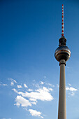 The iconic Fernsehturm in Berlin reaches high, surrounded by a clear blue sky and scattered clouds during the day.