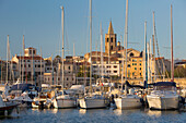 Yachts moored in marina beneath the Old Town walls, sunrise, bell tower of the cathedral prominent on skyline, Alghero, Sassari, Sardinia, Italy, Mediterranean, Europe