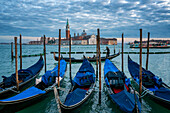 Gondoliere paddeln in einer Gondel mit der Insel San Giorgio Maggiore und der Basilika im Hintergrund bei Sonnenuntergang, Venedig, UNESCO-Weltkulturerbe, Venetien, Italien, Europa