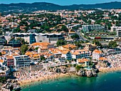 Aerial view of Cascais beaches and colourful rooftops of coastal town under bright sunlight with Sintra mountains in the background, Cascais, Portugal, Europe