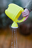 Extreme close up of a boy hand pouring water from a plastic watering can