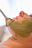 Close up of a brush on a woman face with green beauty mask