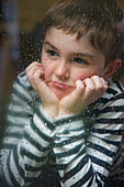 Boy with Hands on Chin behind Rainy Window