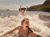 Happy, carefree boy and girl swimming and splashing in sunny ocean waves, Kingstown